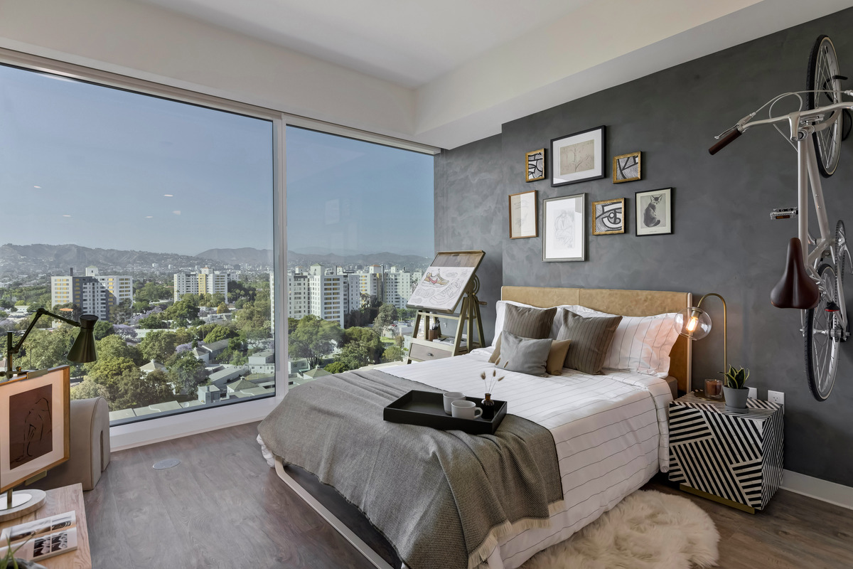 Model Unit Bedroom Featuring Modern Bed and Furniture, Floor-to-Ceiling Windows and a Towering View of the City